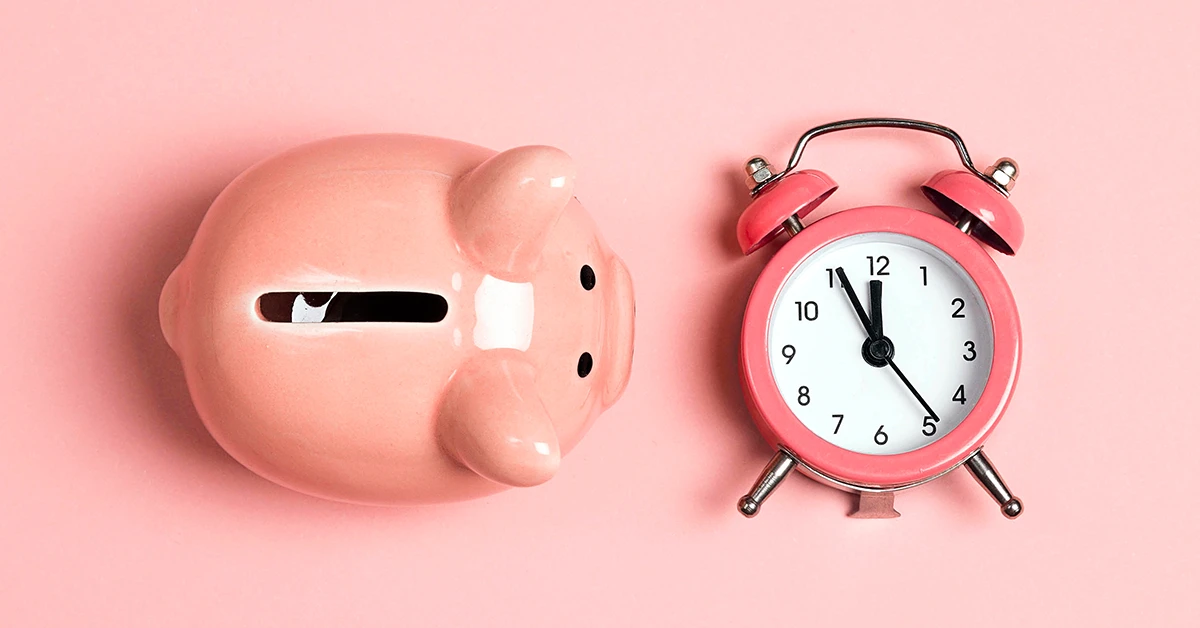 A pink piggy bank and a pink alarm clock lay against a pink background.