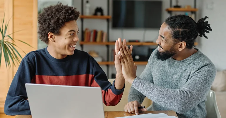 Parent and teenager high-fiving while studying together at home with a laptop