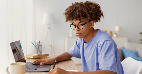High school student studying with a laptop and notebook at a desk, focused on ACT test prep.