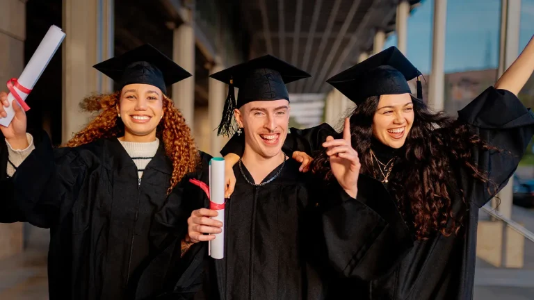 Three students proudly hold their diplomas in the air on graduation day.